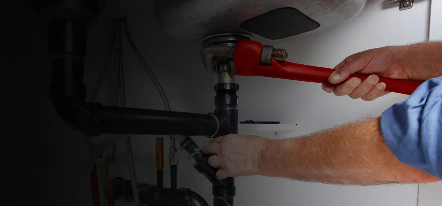 Plumber tightening a pipe under a sink with a red wrench